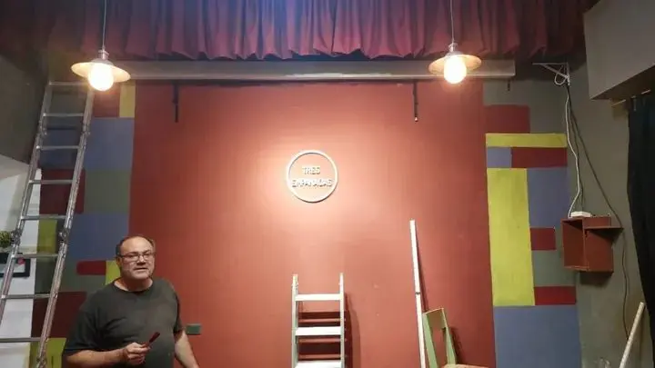 Checho Falco pintando el escenario de Tres Empanadas Comedia, La Plata: paredes con bloques de color y el logo de Tres Empanadas en el centro